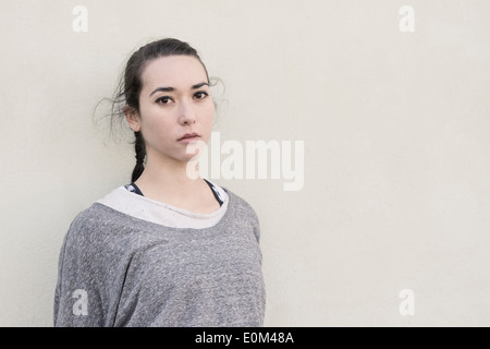 Portrait of young woman standing in front of wall. L'expression rêveuse et à la recherche à l'appareil photo. Banque D'Images