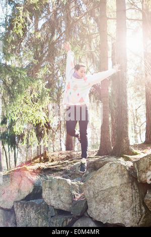 Jeune femme dans la nature de sauter sur le bord de gros rochers dans les bois. Banque D'Images