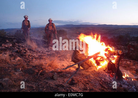 Deux membres de l'équipe Wolf Creek Hotshot réchauffer à côté d'un moignon de genièvre brûlant le matin après une longue nuit, Nouveau Mexique Banque D'Images