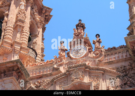 Un gros plan de l'horloge et les figures sculptées en pierre rose sur la façade de l'église de Santa Prisca à Taxco, Mexique Banque D'Images