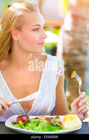 Portrait de jolie femme de manger une salade fraîche et de la viande à l'aide de fourchette et couteau, déjeuner dans un restaurant en plein air Banque D'Images