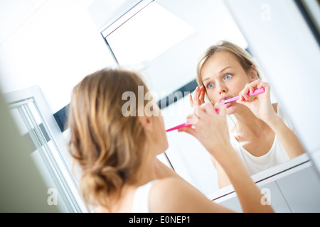 Jolie femme se brosser les dents en face de miroir le matin, faisant de silly faces, contrôler sa peau Banque D'Images