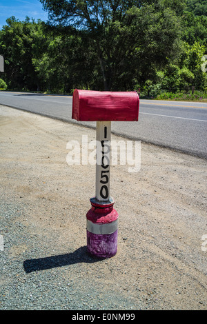 Une boîte aux lettres rouge à côté d'une autoroute du pays. La boîte aux lettres est supporté par d'être cimentés dans une vieille boîte du lait. Banque D'Images