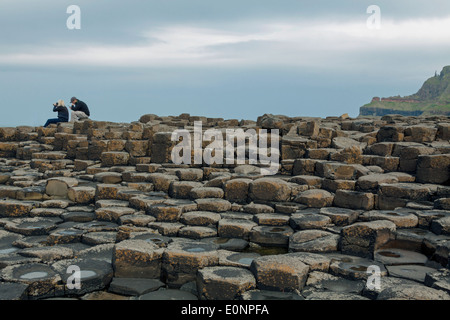 Couple assis sur les pierres de basalte à la Giant's Causeway, County Antrim, Northern Ireland, UK, Site du patrimoine mondial de l'UNESCO. Banque D'Images