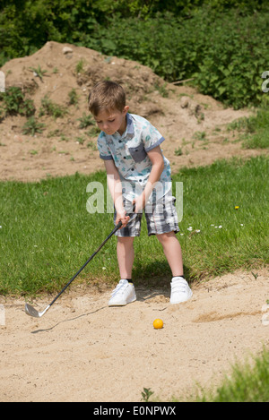 Petit garçon de 5 ans et d'un passionné de golf joue d'un bunker à l'aide d'une taille spécialement coupés golf club. Hampshire Angleterre Banque D'Images