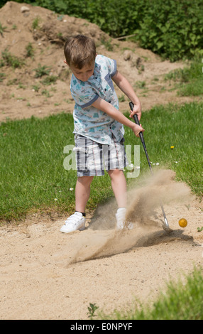 Petit garçon de 5 ans et d'un passionné de golf joue d'un bunker à l'aide d'une taille spécialement coupés golf club. Hampshire Angleterre Banque D'Images