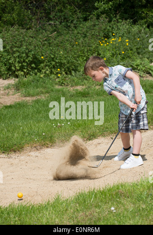 Petit garçon de 5 ans et d'un passionné de golf joue d'un bunker à l'aide d'une taille spécialement coupés golf club. Hampshire Angleterre Banque D'Images