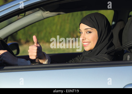 Heureux l'arabie arabe femme conduire une voiture avec thumb up smiling avec un foulard Banque D'Images