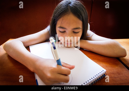 Les jeunes Français / Thai mixed race girl photos avec un stylo dans un livre de dessin à une table dans un restaurant. Banque D'Images