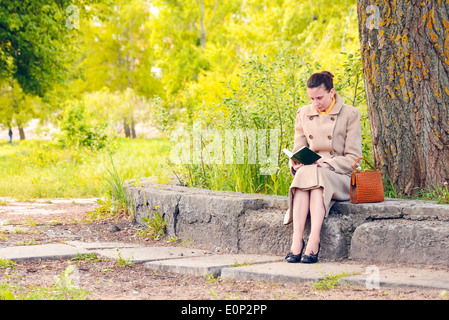 Femme élégante assise sur un mur de pierre au cours d'une journée de printemps ensoleillée, et la lecture d'un livre d'aventure Banque D'Images