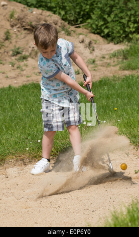 Petit garçon de 5 ans et d'un passionné de golf joue d'un bunker à l'aide d'une taille spécialement coupés golf club. Hampshire Angleterre Banque D'Images