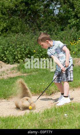 Petit garçon de 5 ans et d'un passionné de golf joue d'un bunker à l'aide d'une taille spécialement coupés golf club. Hampshire Angleterre Banque D'Images