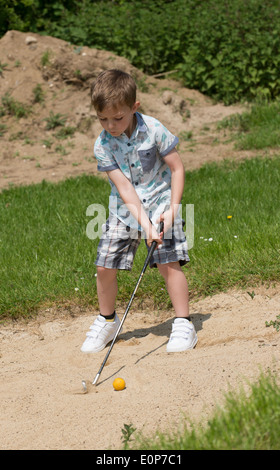 Petit garçon de 5 ans et d'un passionné de golf joue d'un bunker à l'aide d'une taille spécialement coupés golf club. Hampshire Angleterre Banque D'Images