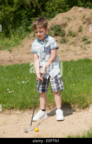 Petit garçon de 5 ans et d'un passionné de golf joue d'un bunker à l'aide d'une taille spécialement coupés golf club. Hampshire Angleterre Banque D'Images