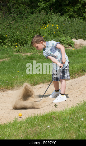 Petit garçon de 5 ans et d'un passionné de golf joue d'un bunker à l'aide d'une taille spécialement coupés golf club. Hampshire Angleterre Banque D'Images