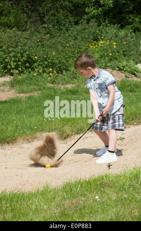 Petit garçon de 5 ans et d'un passionné de golf joue d'un bunker à l'aide d'une taille spécialement coupés golf club. Hampshire Angleterre Banque D'Images