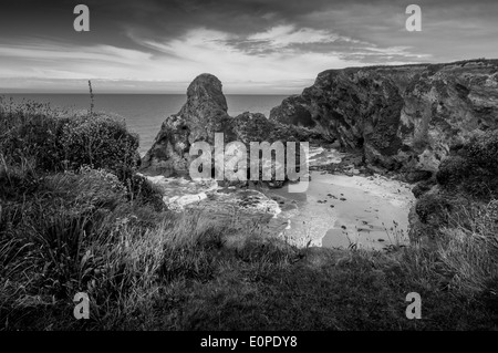 Vista de la falaises accidentées à Newquay en regardant l'océan et sur la plage ci-dessous, avec des volutes au-dessus des nuages gris foncé Banque D'Images