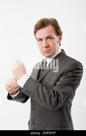 Homme dans un costume d'affaires classique gris réglage de sa chemise brassard, sur un fond blanc. Banque D'Images