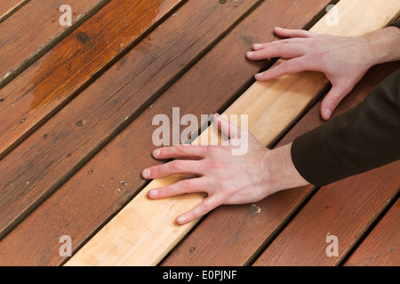 Photo horizontale main d'hommes de mettre en une seule nouvelle planche de bois de cèdre à côté de décoloration sur une terrasse en bois Banque D'Images