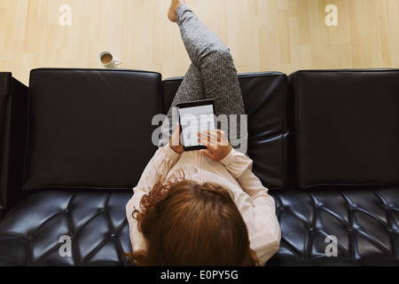 Top View of young brunette using digital tablet while sitting on a couch. Femme lisant un livre Banque D'Images