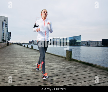 La formation en dehors de coureuse. Athlète féminine caucasienne jogging le long de la rivière de la promenade en ville. Fit young woman running. Banque D'Images