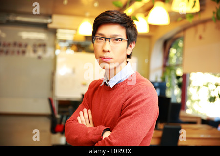 Young happy male student with arms folded standing in classroom Banque D'Images
