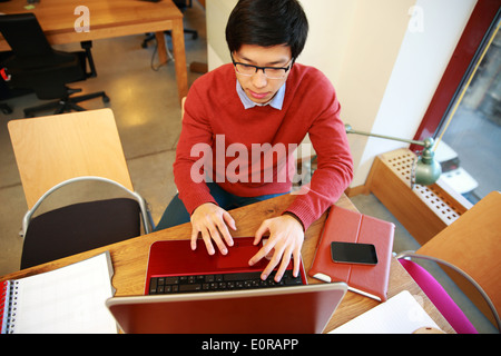 Young Asian man dans les verres working on laptop in office Banque D'Images