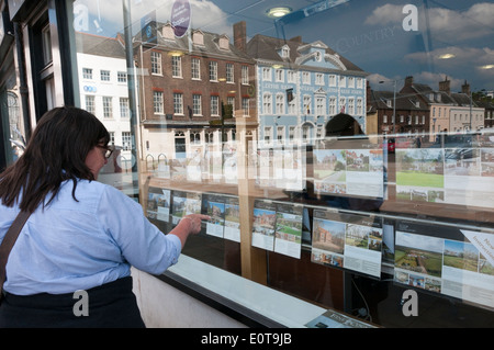 Femme à la fenêtre de l'agent immobilier dans la région de King's Lynn avec réflexion du mardi Marché. Banque D'Images