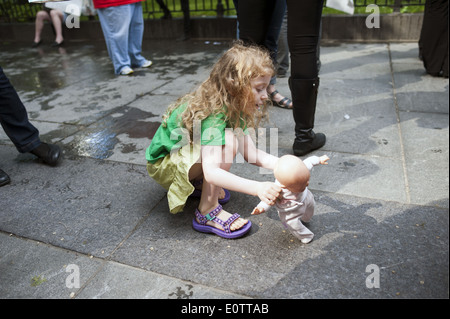 Jeune fille lui enseignant baby doll de marcher sur un trottoir bondé près de New York City Hall Park, 2014. Banque D'Images