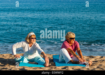 Deux femmes seniors doing stretching exercices sur la plage. Banque D'Images