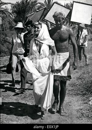 Le 19 octobre 1964 - 19-10-64 Garde côtière dans le désert pour Ursula Andress. Porter des robes qui coule, l'actrice Ursula Andress promenades pour un film situé dans un désert d'Israël avec sa co-star John Richardson à ses côtés. Derrière elle, parmi les techniciens de cinéma, des marches d'un soldat israélien. Il est l'un des soldats envoyés pour protéger les étoiles alors qu'ils sont sur l'emplacement dans le désert pour le film Ã¢â'¬ËoeShe', de toute attaque par des guérilleros armés rôdant à proximité sur la frontière égyptienne. Banque D'Images