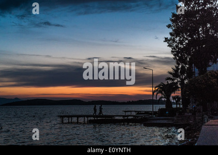 Coucher du soleil sur l'eau face à Foca, Izmir, Turquie District, deux personnes en silhouette marche sur la jetée. Banque D'Images