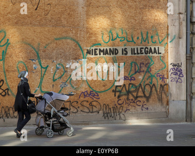 Femme marche en poussant la pram avec graffiti disant personne n'est illégal en langue néerlandaise, Bruxelles, Belgique Banque D'Images