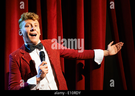 Arts et divertissements dans le théâtre avec funny man travaillant comme présentateur, debout contre des rideaux rouges avec microphone Banque D'Images