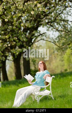 25 avril 2009 - 25 avril 2009 - red hair woman reading book sur banc blanc dans un pré ; shallow DOF Banque D'Images