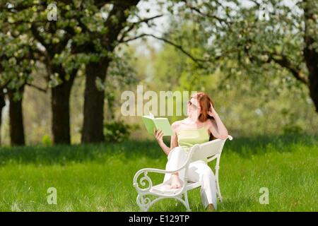 25 avril 2009 - 25 avril 2009 - red hair woman reading book sur banc blanc dans un pré ; shallow DOF Ã'Â© CTK/ZUM Banque D'Images