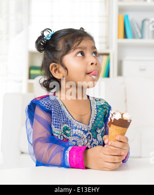 Petite fille indienne de lécher ses lèvres avec un cornet de crème glacée à la main, style de vie familiale à la maison. Banque D'Images