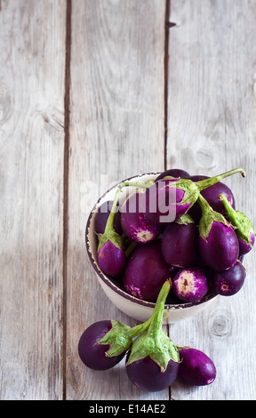 Taille bébé aubergines dans le bol en céramique de table en bois. Focus sélectif. Copie espace arrière-plan. Banque D'Images