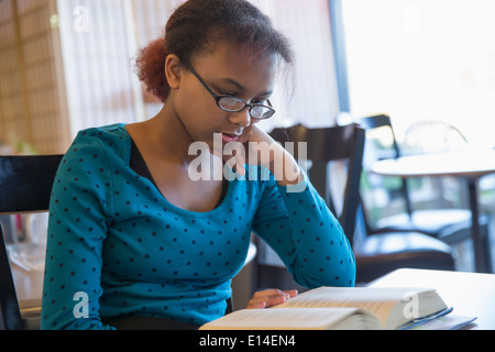 Mixed Race girl reading book in cafe Banque D'Images