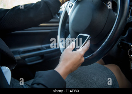 Mixed Race businesswoman using cell phone while driving Banque D'Images