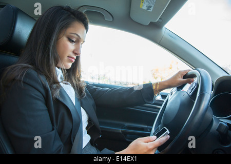 Mixed Race businesswoman using cell phone while driving Banque D'Images