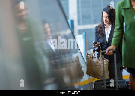 Mixed Race businesswoman using cell phone on escalator Banque D'Images