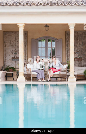 Women toasting each other by swimming pool Banque D'Images
