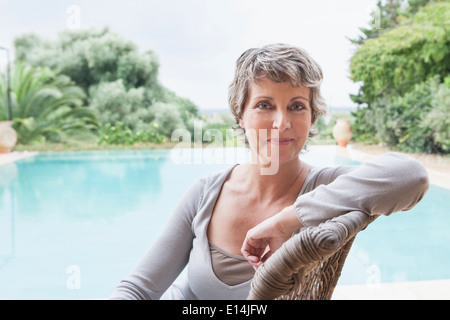 Woman smiling in armchair par piscine Banque D'Images
