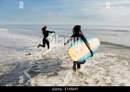 Surfers carrying boards in waves Banque D'Images