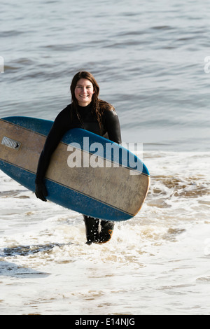 Caucasian surfer carrying board dans les vagues Banque D'Images