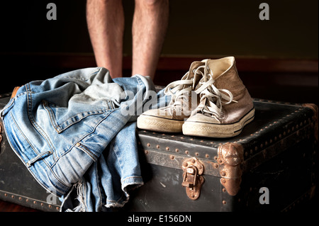 Homme debout derrière valise avec une paire de jeans et baskets sur elle Banque D'Images