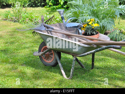 Outils de jardinage dans une brouette avec des fleurs en pot Banque D'Images