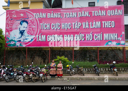 Deux femmes Flower Hmong en permanent de la propagande d'un grand panneau avec Ho Chi Minh en dehors de Bac Ha Bac Ha, Marché, Vietnam Banque D'Images