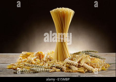 Variété de pâtes alimentaires non cuites sur table en bois avec des épis de blé Banque D'Images